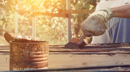 Male worker in old glove is painting the fence boards