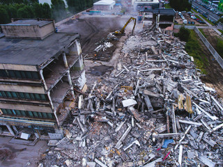 Obraz premium A process of buliding demolition, demolition site with heavy bulldozer and excavator with crushing equipment at work, demolished house, shot from air with drone