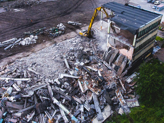 Obraz premium A process of buliding demolition, demolition site with heavy bulldozer and excavator with crushing equipment at work, demolished house, shot from air with drone