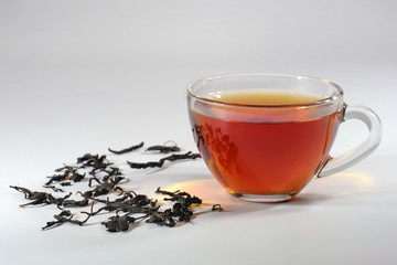 Glass cup of hot tea, and tea leaves on a gray background.