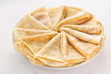 Russian pancakes (crepes) with powdered sugar - traditional Maslenitsa (Shrovetide) meal on white background.