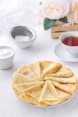 Russian pancakes (crepes) with powdered sugar and sour cream. Traditional Maslenitsa (Shrovetide) meal on white background. Delicious breakfast or brunch with tea.