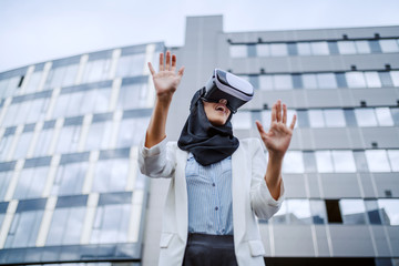 Attractive young muslim businesswoman with scarf on head using vr goggles for virtual presentation....