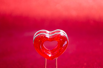 Red heart on a stand in the foreground on a red background with bokeh