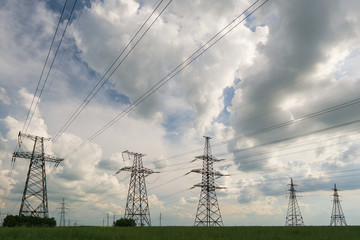 High-voltage power lines passing through a green field, on the background of a beautiful cloudy sky
