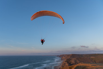 Paraglider flying over thesea shore at sunset. Paragliding sport concept.