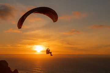 Paraglider flying over thesea shore at sunset. Paragliding sport concept.