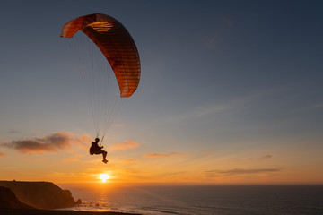 Paraglider flying over thesea shore at sunset. Paragliding sport concept.