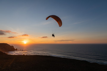 Paraglider flying over thesea shore at sunset. Paragliding sport concept.