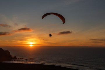 Paraglider flying over thesea shore at sunset. Paragliding sport concept.