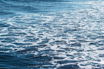 Rippled blue sea water with white foam. Marine texture background.