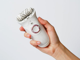 Female epilator white in a female hand on a white background. Electric hair removal device. Concept of skin care and female beauty. Women's suffering. - obrazy, fototapety, plakaty