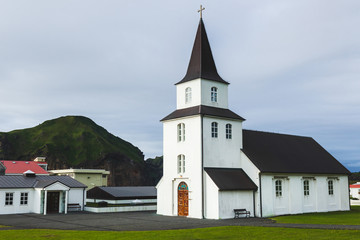 Fototapeta na wymiar Church with Black roof and white walls in traditional nordic minimalist style on Vestmannaeyjar Heimaey island in Iceland. Simple architecture, green grass, nobody around.