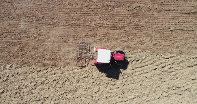 Aerial shot from a birds view of a tractor with a spike tooth harrow cutting through clods, manure, and grasses to break up material into finer pieces so that it can be spread evenly across the ground
