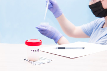 a jar with sperm, stand on a 500 euros, a sperm donor concept, female hands with a pipette and a jar for analysis in the background in blue gloves, blue background, copy space, paper and pen