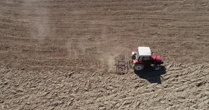 Aerial footage of a tracktor with a spike tooth harrow cutting through clods, manure, and grasses to break up material into finer pieces so that it can be spread evenly across the ground