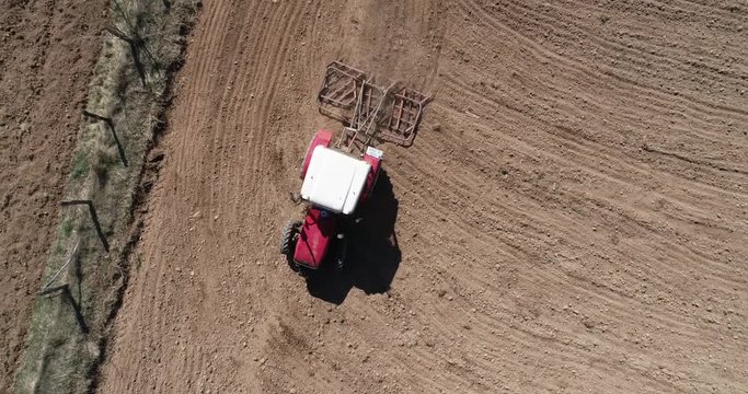 Aerial footage of a tracktor with a spike tooth harrow cutting through clods, manure, and grasses to break up material into finer pieces so that it can be spread evenly across the ground