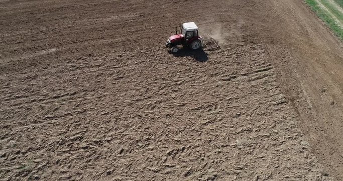 Aerial footage of a tracktor with a spike tooth harrow cutting through clods, manure, and grasses to break up material into finer pieces so that it can be spread evenly across the ground