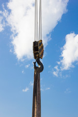 Black and yellow cargo crane hook with slings, against a blue sky with clouds