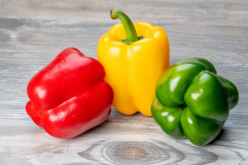 Three colored bell peppers on a wooden table surface