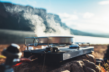 camping cooking in nature outdoor, prepare breakfast picnic in mist morning; cooker food metal gas stove on stone; tourism recreation outside; campsite lifestyle