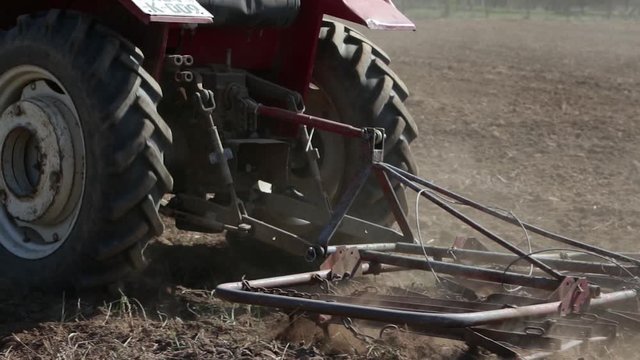 Footage of a tractor aligning the earthy surface on a field with a spike tooth harrow and preparing it for sowing