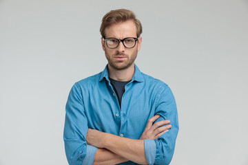 upset young casual guy crossing arms on grey background