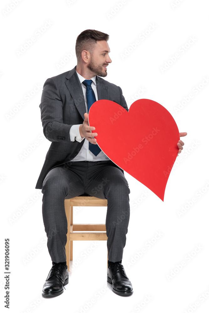 Wall mural elegant businessman holding big red heart and looking to side