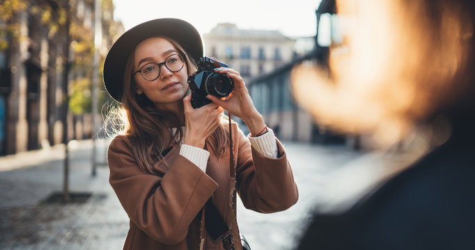 Hobby photographer concept copy space. Outdoor lifestyle portrait of pretty young woman in sun city in Europe with camera travel photo of photographer Making pictures in glasses and hat