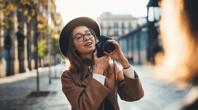 Hobby photographer concept. Outdoor lifestyle portrait of smiling  woman having fun in sun city in Europe with camera travel photo of photographer in glasses and hat take photo model