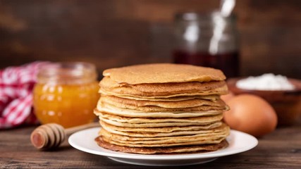 Blini or crepes with honey and jam on rustic wooden table. Stop motion animation of stack of Russian blinis, thin pancakes or crepe. 4k Resolution - Powered by Adobe