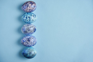 Beautiful blue easter eggs lie in a row on a blue paper background.