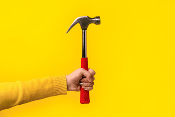 hammer in female hand over yellow background