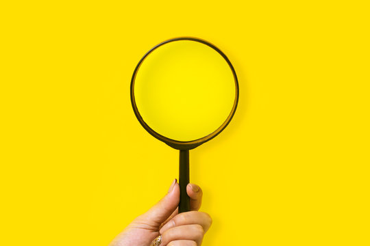 Hand Holding Magnifier Over Yellow Background