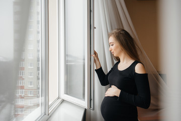 Fototapeta na wymiar A pregnant girl opens a window to get some fresh air