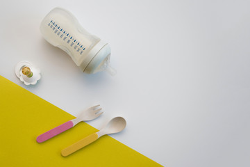 Set of bright baby spoon and fork on table with feeding bottle and nipple. Top view