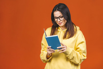 Beautiful young woman wearing casual standing isolated over orange background, reading a book.