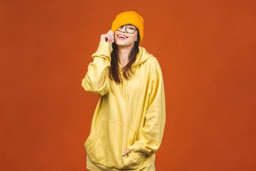 People, youth, leisure and lifestyle concept. Fashionable beautiful young Caucasian young female student wearing stylish clothing laughing, pointing finger. Isolated over orange.