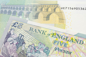 A five pound British pound sterling with a red, five Euro European bank note close up in macro