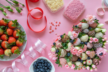 Handmade chocolate covered strawberries, flowers and decoration for cooking dessert on pink background