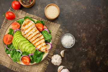 Grilled chicken breast and fresh vegetable salad with spinach leaves, avocado and tomatoes on a...