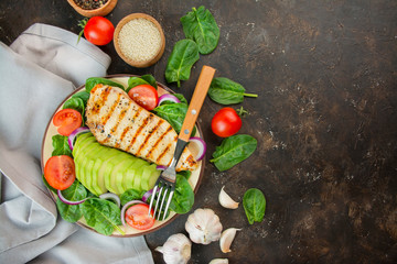 Grilled chicken breast and fresh vegetable salad with spinach leaves, avocado and tomatoes on a...