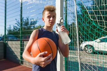 Boy teenager basketball player with ball drinking water from bottle
