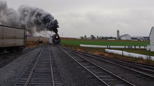Head on View of a Steam Locomotive Pulling Freight Pulling into Yard with Smoke and Steam on a Rainy Day
