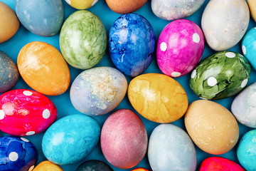 Different easter eggs with straw on wooden plate on blue table
