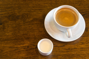 Cup of coffee on wooden table in restoran or coffee house. White ceramic cup view above with copy space