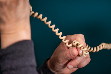Old retro, old fashioned white telephone cord against green background, woman hand holding telephone cord