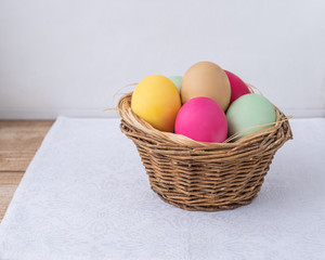 Painted colored natural eggs lie in a small rough rustic basket on a white napkin .