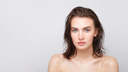 Young candid girl with long wet hair and bare shoulders looks at the camera. Close up portrait against white background