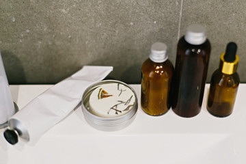 Ubtan for skin in glass bottle, solid shampoo in metal can, tonic,  conditioner on white sink in modern bathroom. Zero waste concept. Plastic free hygiene essentials. Sustainable lifestyle